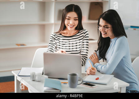 Making notes. Young dark-haired woman wearing glasses feeling attentive making notes listening to her colleague Stock Photo