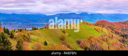 Autumn sunset wide panorama with Saints Primus and Felician Church on top of hill in Jamnik, Slovenia countryside and pink clouds Stock Photo