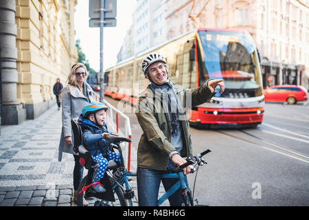 A small toddler boy sitting in bicycle seat with young parents outdoors in city. Stock Photo