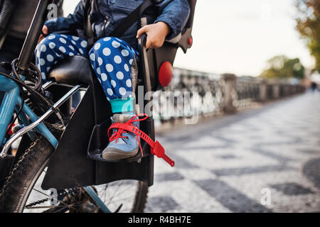 A small toddler boy sitting in bicycle seat outdoors in city. Copy space. Stock Photo