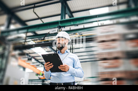 A portrait of an industrial man engineer with clipboard standing in a factory. Stock Photo