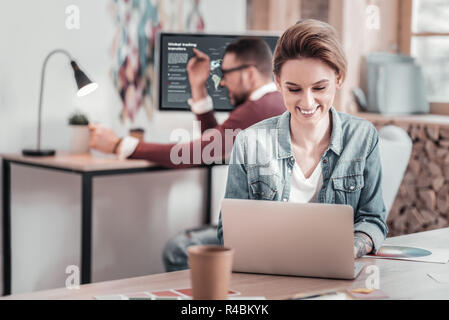Lets chat. Kind young female person looking at screen of laptop while having pleasant communication Stock Photo