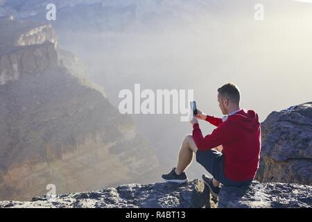 Relaxation in mountains. Young man photographing by mobile phone. Jebel Akhdar, Grand Canyon of Oman. Stock Photo