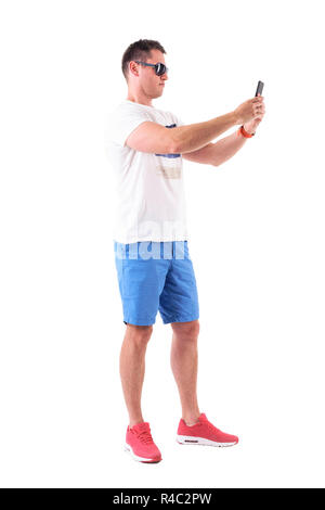 Young handsome male tourist taking photo with mobile phone in summer clothes. Full body isolated on white background. Stock Photo