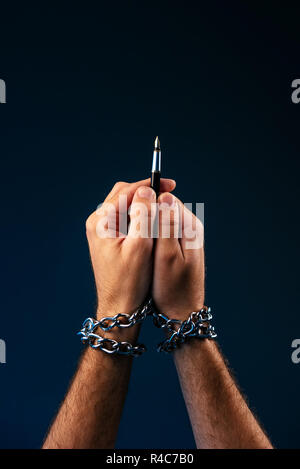 Freedom of the press and journalism, conceptual image with pen in male hand tied with chains, low key image Stock Photo