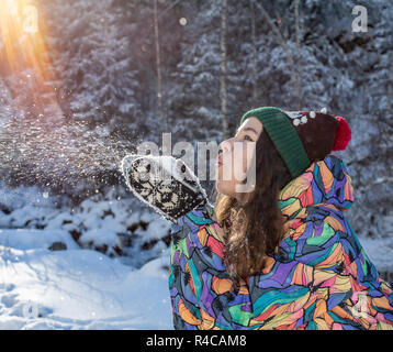 Beauty Winter Girl Blowing Snow in frosty winter Park. Outdoors. Flying Snowflakes. Sunny day. Backlit. Joyful Beauty young woman Having Fun in Winter Park. Stock Photo