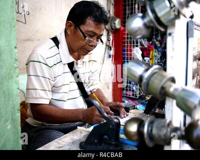 ANTIPOLO CITY, PHILIPPINES - NOVEMBER 24, 2018: A locksmith and rubber stamp maker works on his makeshift shop at a sidewalk along a busy street. Stock Photo