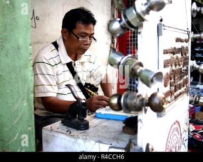 ANTIPOLO CITY, PHILIPPINES - NOVEMBER 24, 2018: A locksmith and rubber stamp maker works on his makeshift shop at a sidewalk along a busy street. Stock Photo