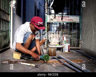ANTIPOLO CITY, PHILIPPINES - NOVEMBER 24, 2018: A worker uses a grinder to trim a metal rod which he will use to build a fence for a house. Stock Photo