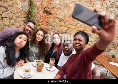 Friends making faces and taking selfies in a cafe courtyard Stock Photo