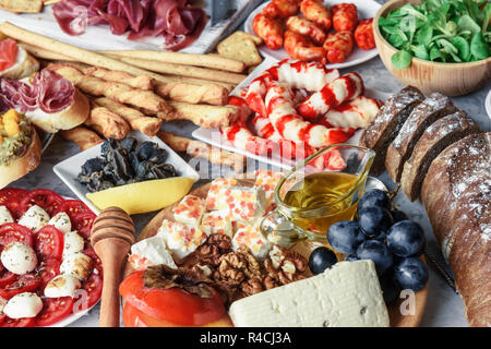 Italian antipasti snacks set. Brushettas, cheese variety, shrimps, salmon, olives, prosciutto with pear, salami and jamon over grey grunge table Stock Photo
