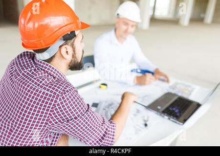 male engineers, architects working at the desk in helmets. Drawings, laptop, roulette on the desktop. Reception and supervision of building constructi Stock Photo