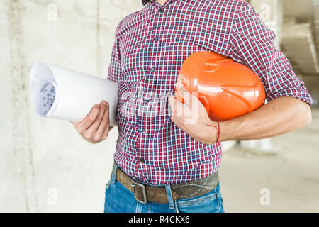 male engineer, architect in helmet at construction site holds drawing on paper in hands Stock Photo