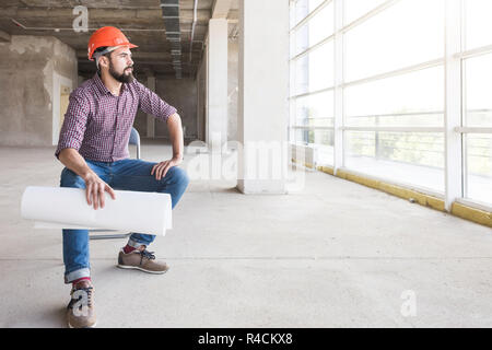 the man is an engineer in a helmet, in a checkered shirt with paper with drawings, in the construction being completed. building supervision Stock Photo