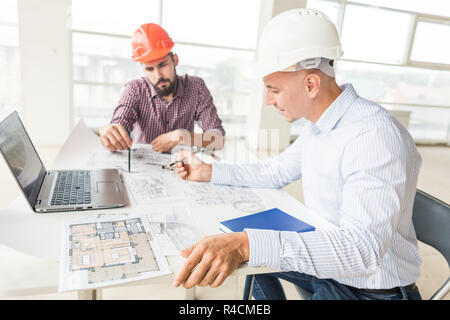 male engineers, architects working at the desk in helmets. Drawings, laptop, roulette on the desktop. Reception and supervision of building constructi Stock Photo