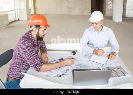 male engineers, architects working at the desk in helmets. Drawings, laptop, roulette on the desktop. Reception and supervision of building constructi Stock Photo