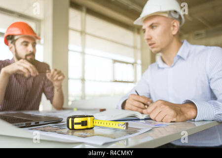 male engineers, architects working at the desk in helmets. Drawings, laptop, roulette on the desktop. Reception and supervision of building constructi Stock Photo