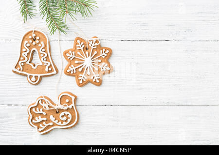 Christmas Gingerbread cookies are hanging on spruce branch over white wooden background with copy space. Handmade decorations. Stock Photo