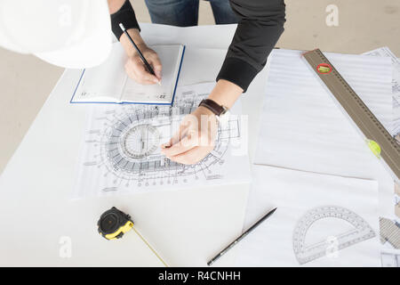 architect builder works at the table with drawings. Helmet, drawings, compasses in the workplace Stock Photo