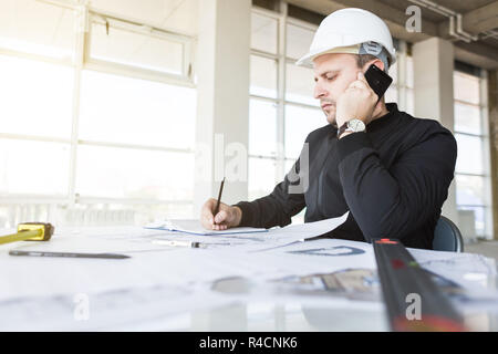 architect builder works at the table with drawings. Helmet, drawings, compasses in the workplace Stock Photo