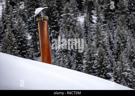 mountain house roof with smoking chimney on the deep white snow background Stock Photo