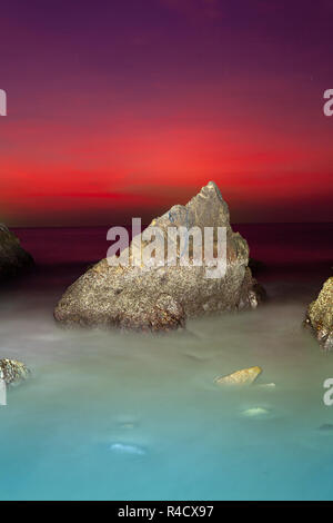 waves hit the big cone shape rock in the middle of stone cape during sunset at banana beach Phuket Stock Photo