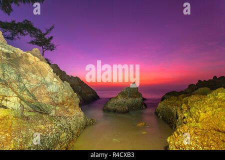 waves hit the big cone shape rock in the middle of stone cape during sunset at banana beach Phuket Stock Photo