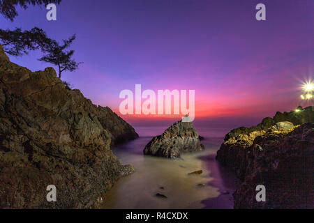 waves hit the big cone shape rock in the middle of stone cape during sunset at banana beach Phuket Stock Photo