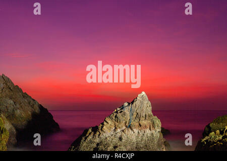 waves hit the big cone shape rock in the middle of stone cape during sunset at banana beach Phuket Stock Photo