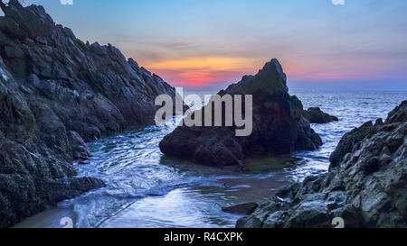 waves hit the big cone shape rock in the middle of stone cape during sunset at banana beach Phuket Stock Photo