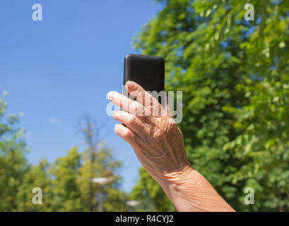 The phone in hand of old woman on the blue sky background Stock Photo
