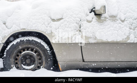 Fragment of a car covered with a thick layer of snow. Front wheel and rearview mirror area. Winter weather background Stock Photo