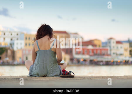 Rear view of woman sitting on a pier, reading book. Stock Photo