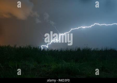 A powerful horizontal lightning bolt curves and strikes down to the earth. This special lightning bolt has side branches pointing upward into the air. Stock Photo