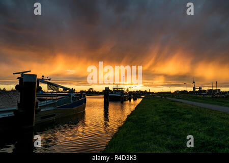 Harbor in Gouda, Holland with colorful sunset. Rain streaks at the back of a cold front are beautifully illuminated by the setting sun. Stock Photo