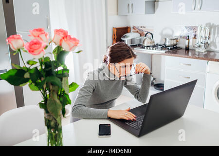 Woman talking working on laptop on modern kitchen. Angry irritated freelancer staring at screen taking glasses off Stock Photo