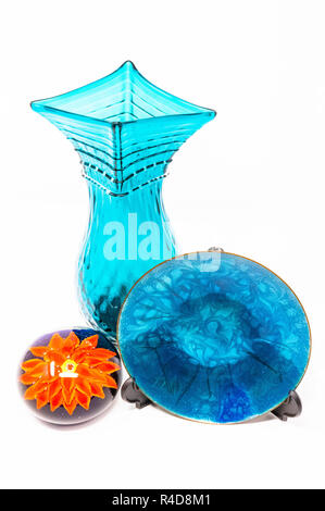 A blue glass vase and plate against a white background with an orange flower glass paperweight. Stock Photo