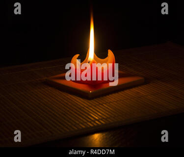 Red candle on bamboo mat with reflection in glossy table with black background. Stock Photo