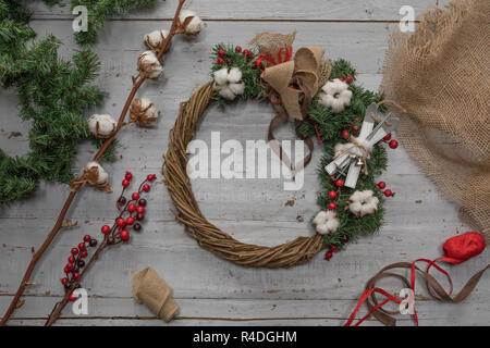 Top view of stages of making Christmas wreath with fir branches and decorative toys on wooden rustic tabletop Stock Photo