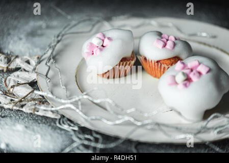 sweet winter cupcakes with white, light sugar foam and pink marshmallows on the background of a Christmas decoration with snow Stock Photo