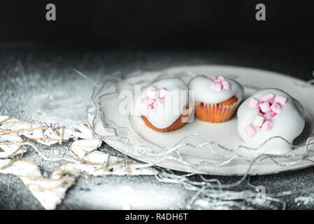 sweet winter cupcakes with white, light sugar foam and pink marshmallows on the background of a Christmas decoration with snow Stock Photo