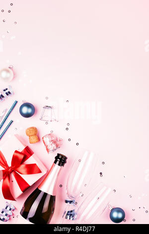 Christmas gift with red bow, bottle of champagne, two glasses and blue decorationson pink background. Beautiful holiday composition. Vertical background with copy space. Stock Photo