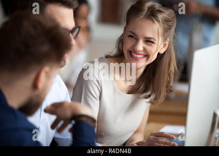 Smiling young woman talking with colleagues at shared workplace Stock Photo