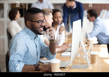Smiling African American man talking by phone, using computer Stock Photo