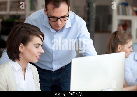 Middle aged mentor helping female employee with computer work Stock Photo