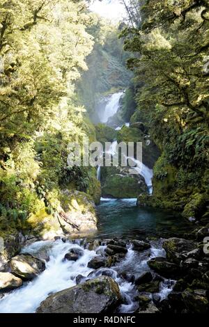 Waterfall going over big rocks and green trees surrounding it,  Milford Track New Zealand South Island Stock Photo