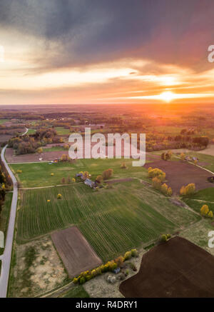 Aerial Drone Photograph of a  Village Surrounded with  Meadows  in Beautiful Spring Colours in Evening with Sunset Over it Stock Photo