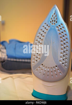 closeup vertical shot of iron with stack of folded shirts on ironing board blurred on background Stock Photo
