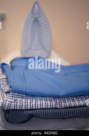 pile of fresh clothes dress shirts with iron blurred on background. selective focus on foreground Stock Photo