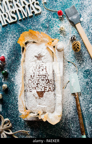Chocolate banana bread with a christmas tree decor and a small wooden spatula on the sidelat lay  over a rustic green and blue background, top view. Stock Photo